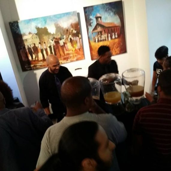 A group of people gathered around in front of paintings.