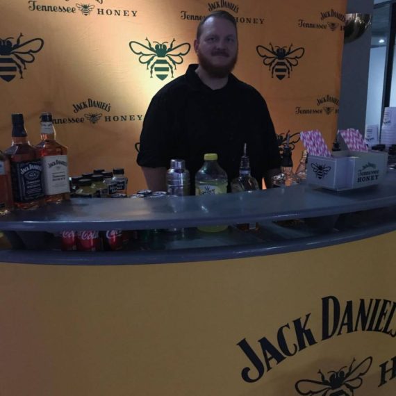 A man standing behind the bar of a jack daniels honey bar.