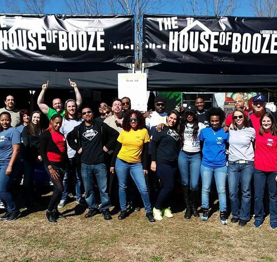 A group of people standing in front of a house of booze tent.